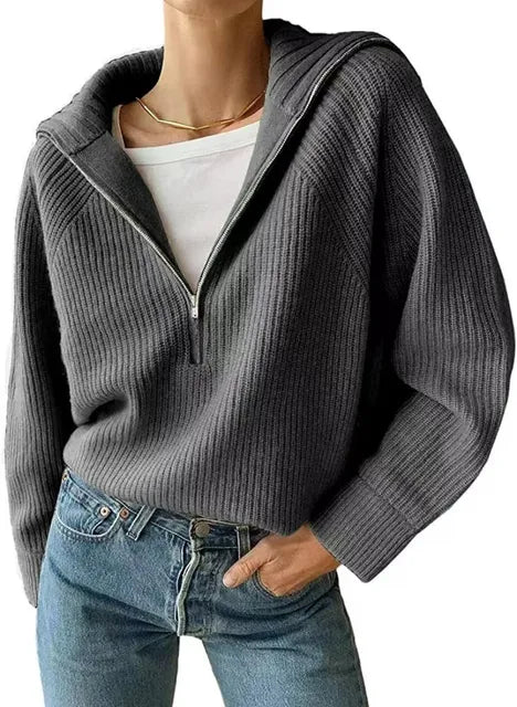 Femme portant un pull gris à col zippé, manches longues, en maille côtelée, avec un t-shirt blanc et un jean bleu. Mode décontractée élégante.