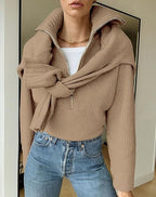 Femme portant un pull beige en maille avec un col zippé, noué autour des épaules, et un jean bleu. Mode automne, style décontracté chic.