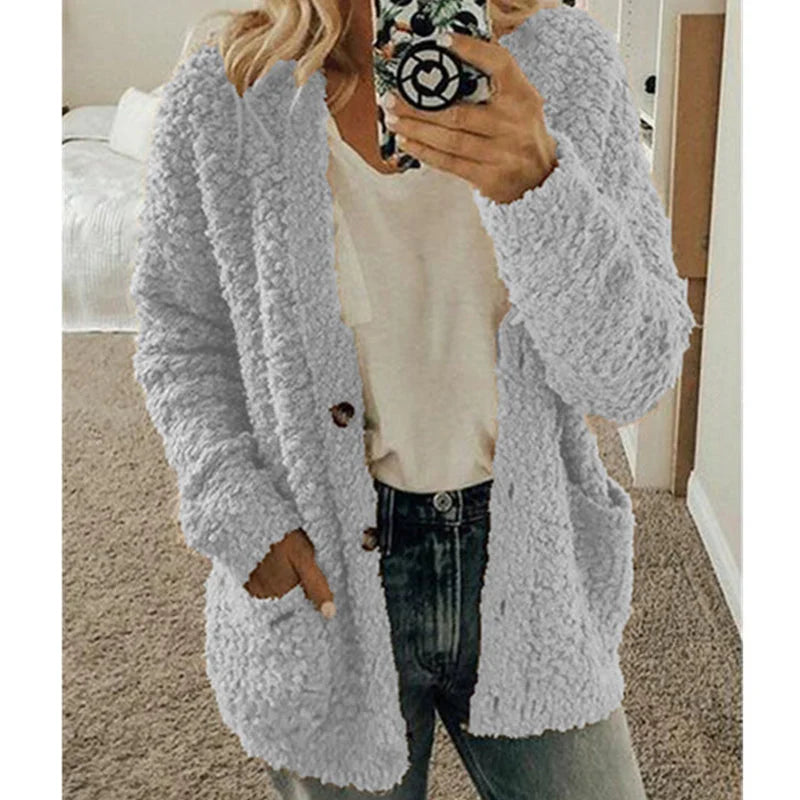 Femme portant un cardigan en laine bouclée gris, tenue décontractée avec jean et t-shirt blanc, tenant un smartphone. Mode automne-hiver tendance.