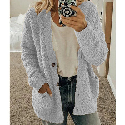 Femme portant un cardigan en laine bouclée gris, tenue décontractée avec jean et t-shirt blanc, tenant un smartphone. Mode automne-hiver tendance.