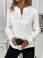 Femme portant un pull blanc texturé, tenant un gobelet de café noir. Mode automne, style décontracté, tendance féminine, intérieur moderne.