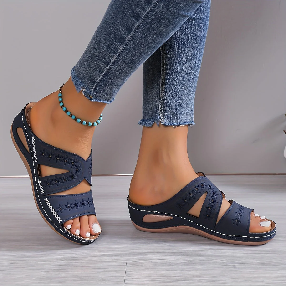 Sandales bleues pour femme avec motifs découpés, portées avec un jean effiloché et un bracelet de cheville turquoise. Mode estivale décontractée.