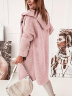 Femme portant un manteau rose en tricot, sac à main beige, posant devant des portraits artistiques en noir et blanc, style moderne et chic.