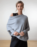 Femme portant un pull gris oversize élégant, avec une épaule dénudée, sur une robe noire. Mode automne-hiver, style décontracté chic.