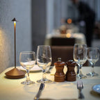 Table de restaurant élégante avec verres à vin, salière, poivrière et lampe moderne. Ambiance raffinée, dîner romantique, décoration chic.