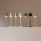 Sept lampes de table modernes alignées, aux abat-jours colorés et design minimaliste, éclairant une surface blanche. Éclairage intérieur contemporain.
