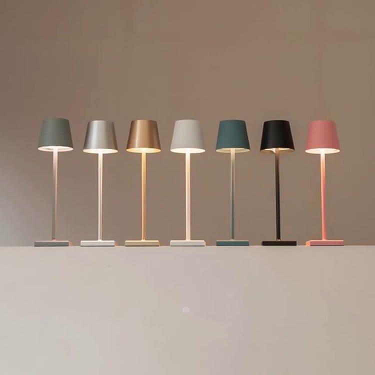 Sept lampes de table modernes alignées, aux abat-jours colorés et design minimaliste, éclairant une surface blanche. Éclairage intérieur contemporain.