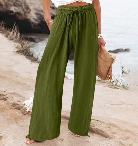 Pantalon large vert kaki femme, style décontracté, plage en arrière-plan, mode estivale, tenue confortable, bord de mer, accessoire sac en paille.