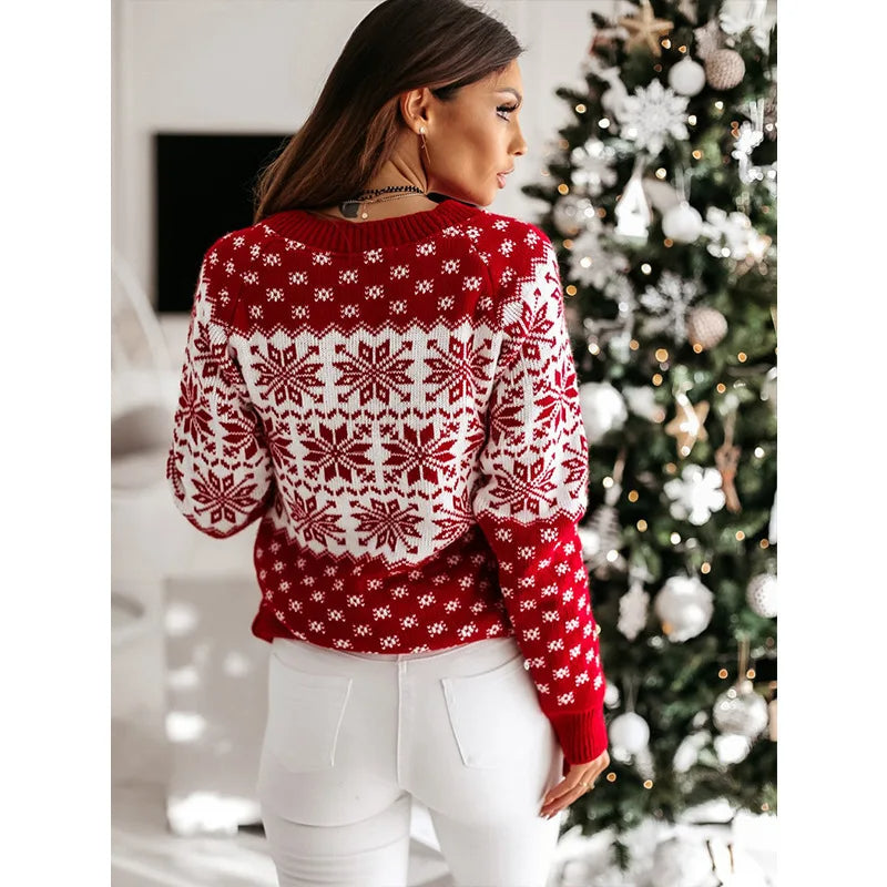 Femme portant un pull rouge à motifs flocons de neige blancs, debout devant un sapin de Noël décoré. Mode hiver, tenue festive, ambiance Noël.