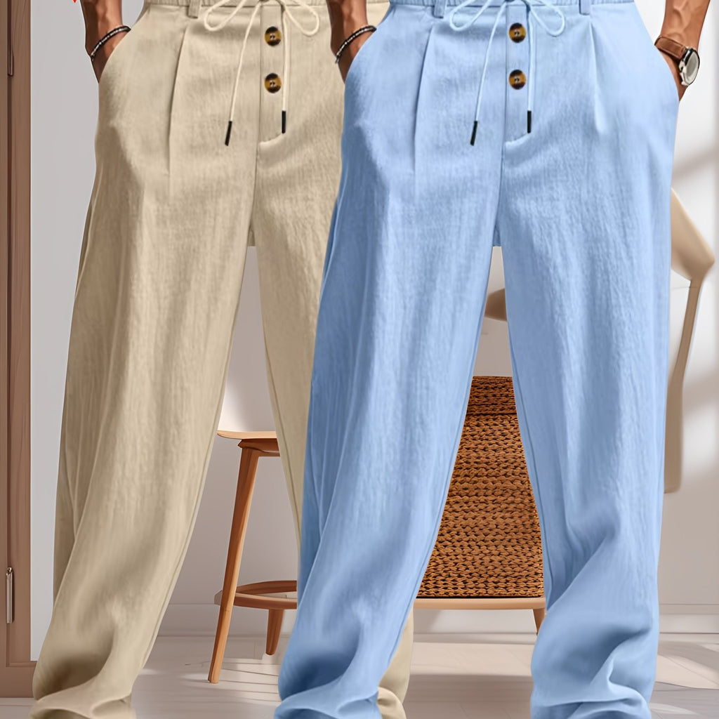 Deux pantalons en lin pour hommes, beige et bleu, avec cordon de serrage et boutons en bois, suspendus dans un intérieur moderne et lumineux.