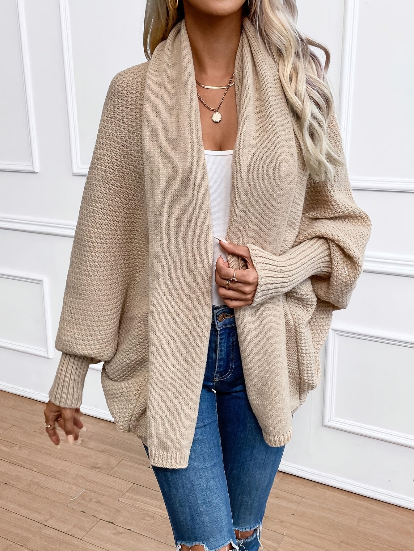 Femme portant un cardigan beige en tricot, style décontracté, avec un jean déchiré. Mode automne-hiver, tenue élégante et confortable.