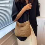 Femme portant un sac en paille tressée, tenue élégante avec veste noire et jupe blanche, mode estivale chic, accessoires tendance.