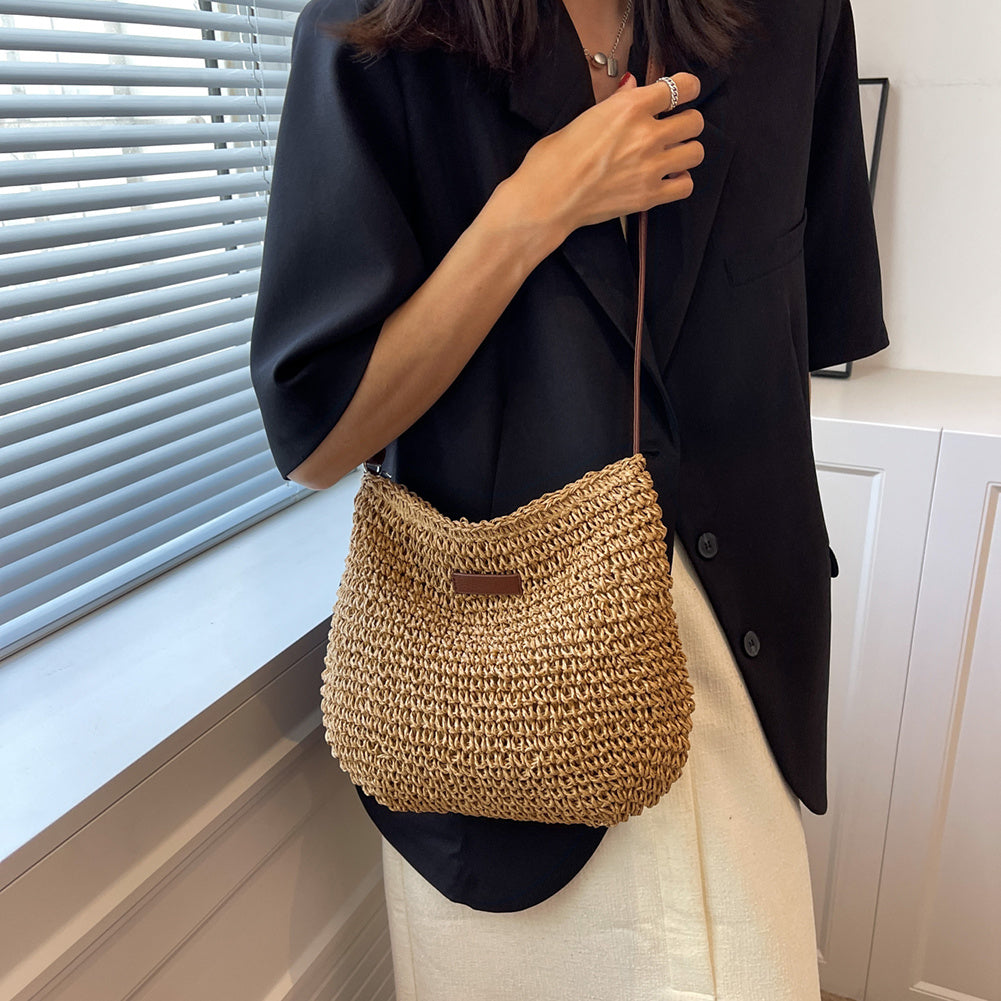 Femme portant un sac en paille tressée, tenue élégante avec veste noire et jupe blanche, mode estivale chic, accessoires tendance.