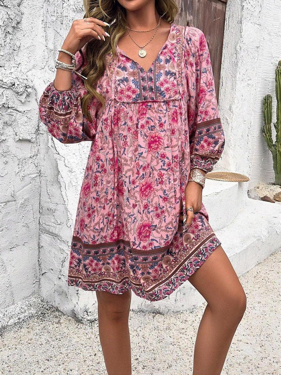 Robe bohème rose à motifs floraux, manches longues, portée par une femme. Style décontracté, idéal pour l'été. Fond blanc avec cactus.