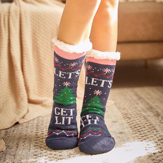 Chaussettes de Noël bleues avec sapins verts et texte "Let's Get Lit", portées sur un tapis beige. Accessoire festif et confortable pour l'hiver.