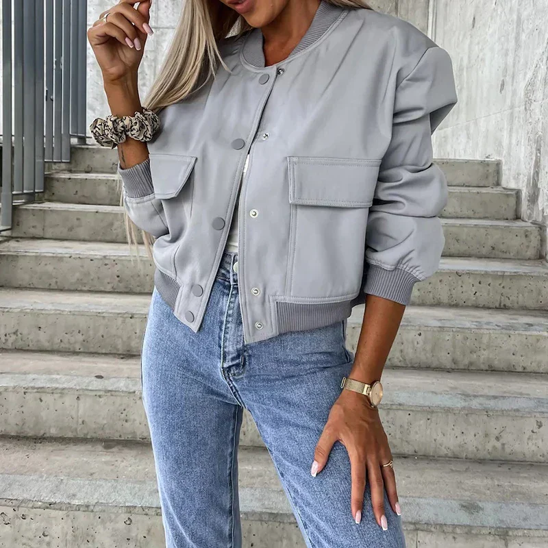 Femme portant un blouson gris tendance avec poches, jean décontracté, montre dorée et chouchou, posant sur des escaliers en béton.