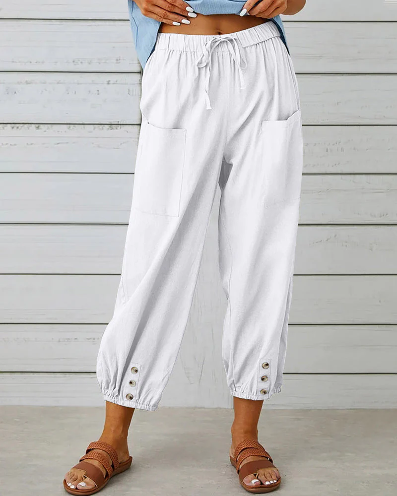 Pantalon blanc ample pour femme avec poches avant, taille élastique et boutons décoratifs, style décontracté estival, porté avec sandales marron.