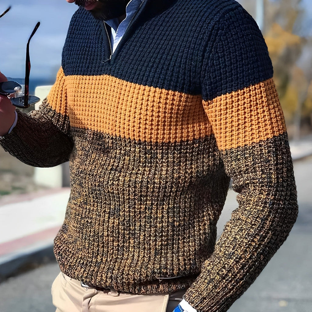 Homme portant un pull en tricot à rayures bleu marine, orange et marron, tenant des lunettes de soleil. Mode automne-hiver, style décontracté.
