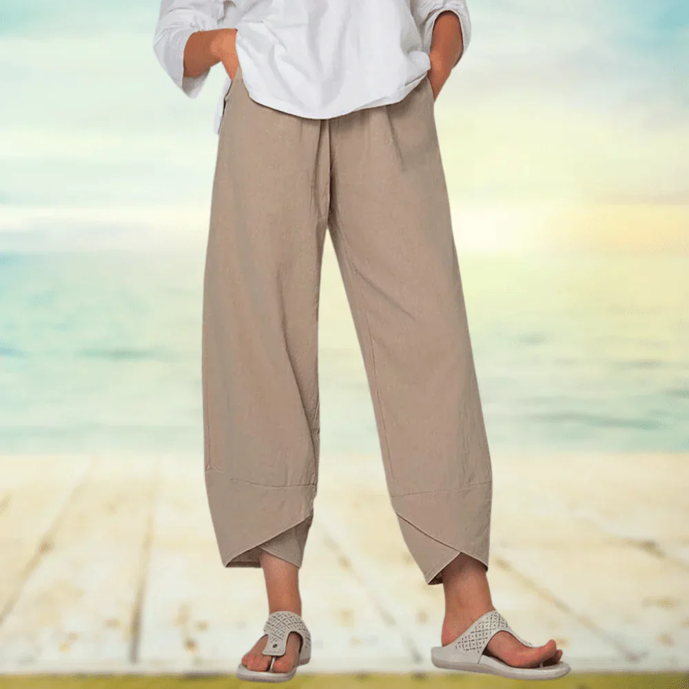 Pantalon beige ample en lin, style décontracté, porté avec une chemise blanche, sur fond de plage ensoleillée. Mode estivale, confort, élégance.