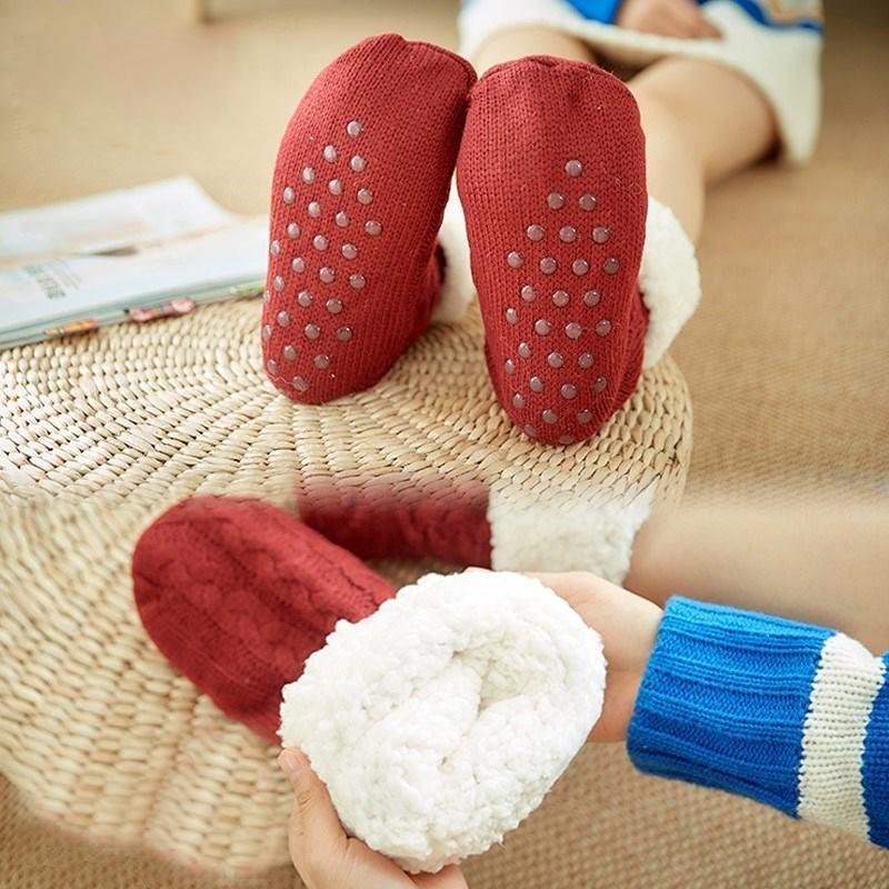 Chaussons rouges antidérapants en tricot, doublés de fourrure blanche, posés sur un tabouret en osier. Accessoire confortable pour l'hiver.