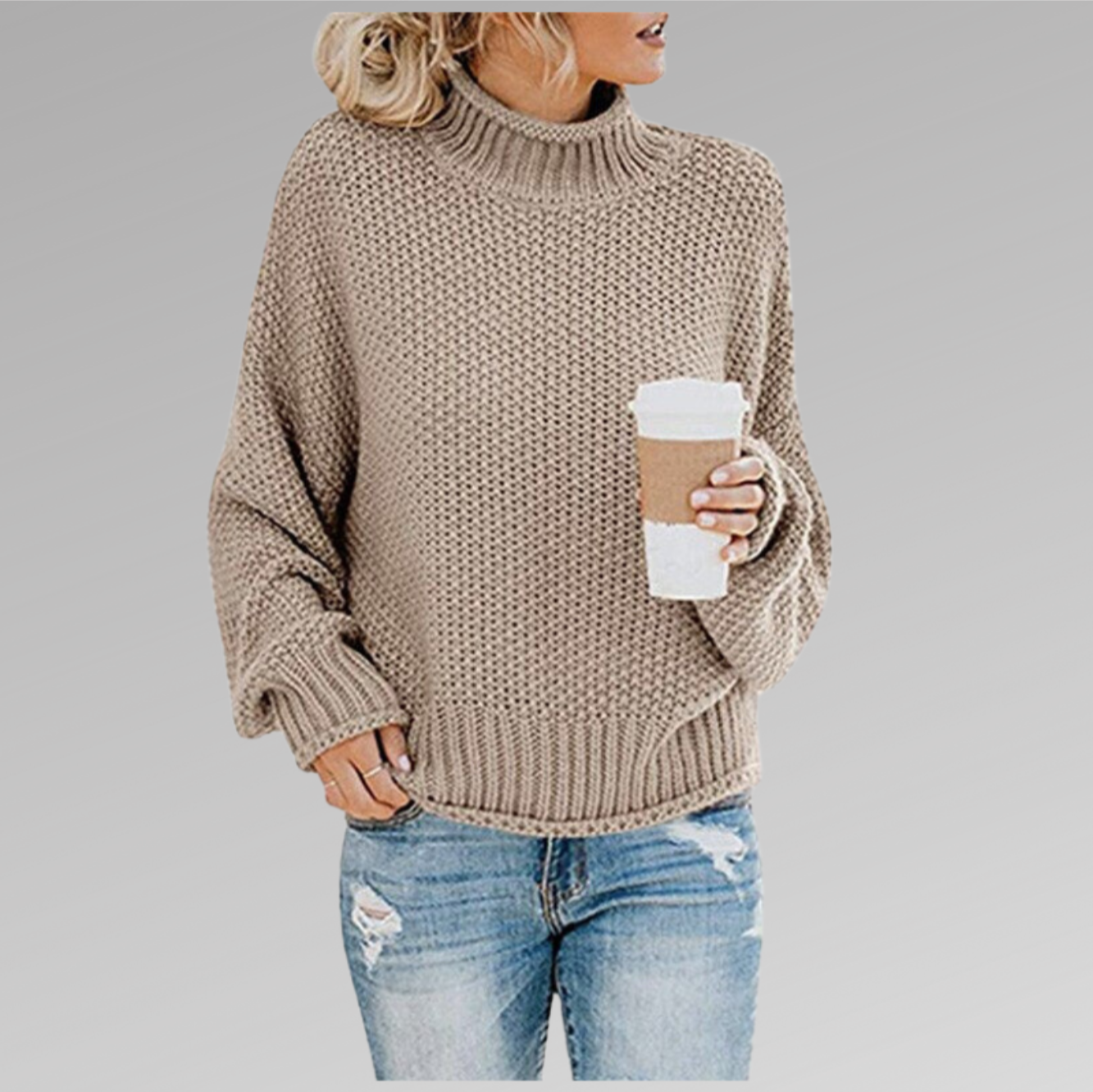 Femme en pull en maille beige, tenant un gobelet de café, portant un jean déchiré. Mode automne, style décontracté, tendance féminine.