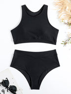 Maillot de bain deux pièces noir, style sportif, sur fond blanc avec lunettes de soleil et feuilles. Mode plage, été, tendance féminine.