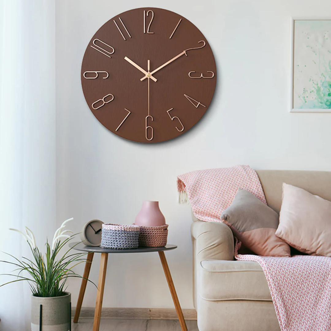 Horloge murale marron moderne avec chiffres dorés, accrochée dans un salon élégant avec canapé beige, coussins et table en bois.