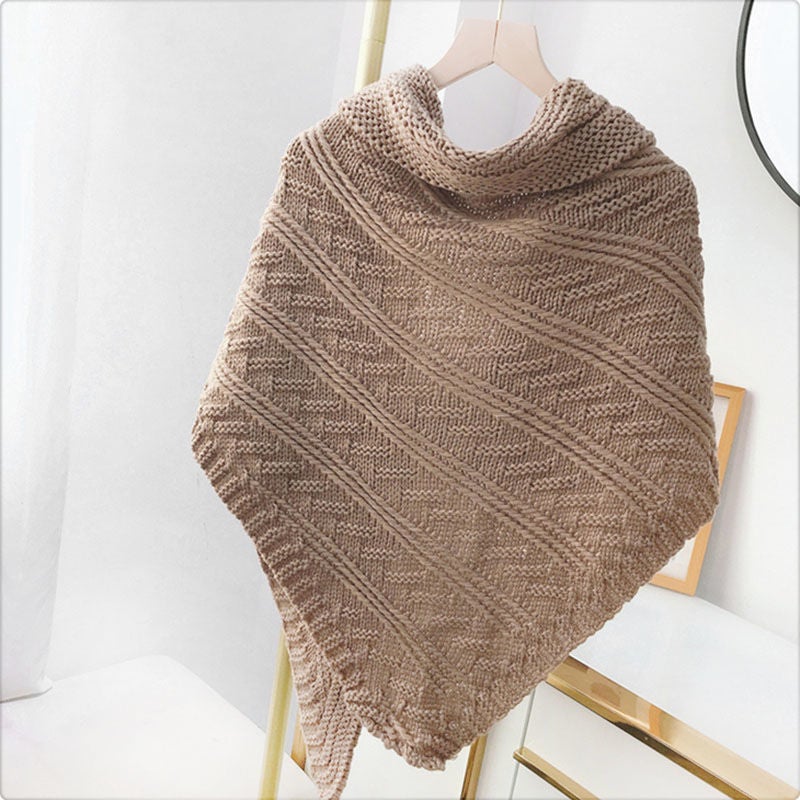 Châle en tricot beige suspendu sur un cintre, motif géométrique, texture douce et élégante, idéal pour l'hiver et la mode féminine.