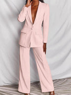 Femme portant un tailleur pantalon rose pâle élégant, veste à bouton unique, sur fond neutre. Mode féminine chic, tenue professionnelle moderne.