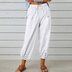 Pantalon blanc ample pour femme avec poches avant, taille élastique et boutons décoratifs, style décontracté estival, fond en bois clair.
