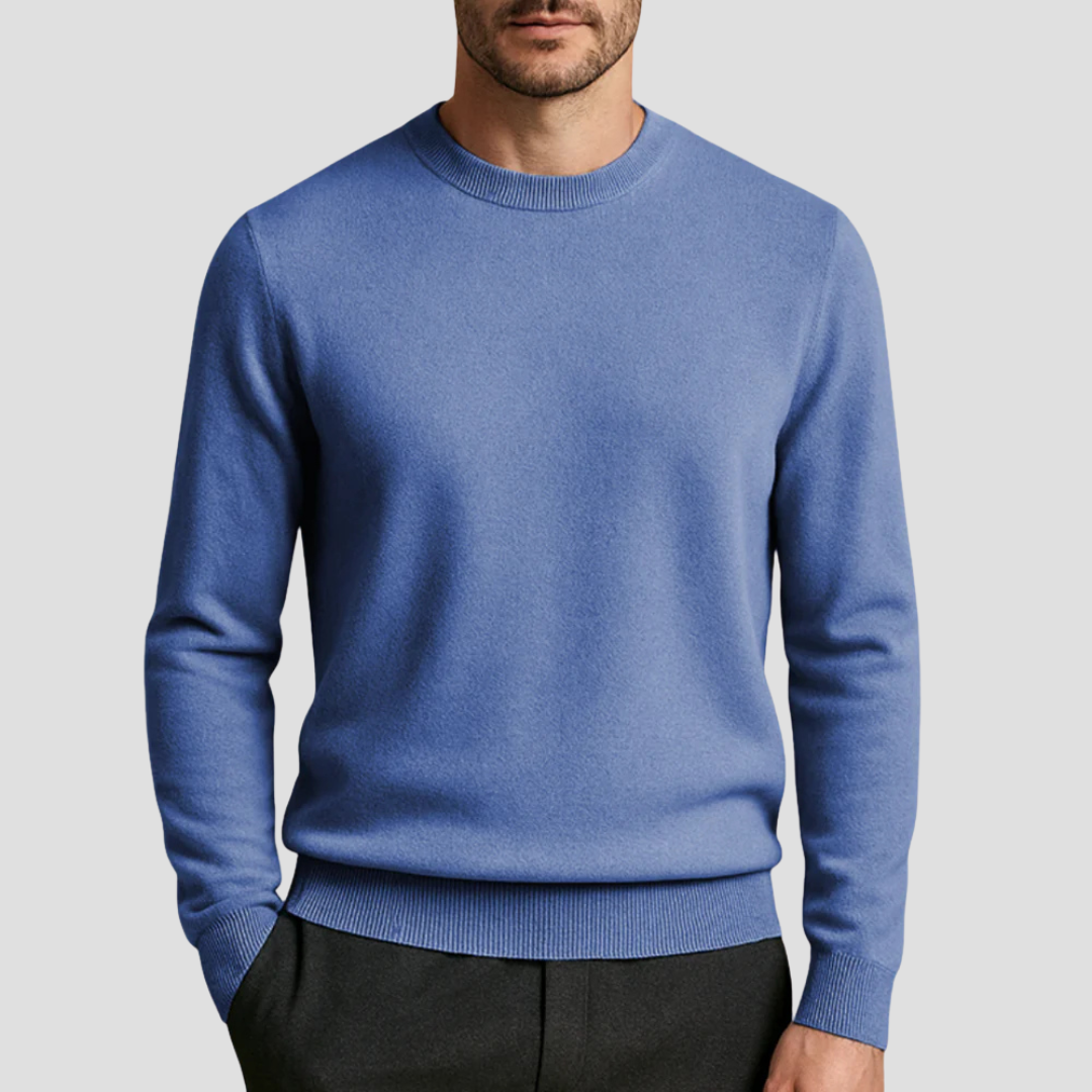 Homme portant un pull bleu en laine, col rond, manches longues, avec pantalon noir. Mode masculine élégante, tenue automne-hiver.