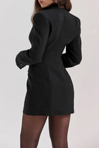 Femme portant une robe blazer noire élégante, manches longues, ajustée, avec collants noirs. Mode chic, tenue de soirée tendance.