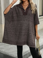 Femme portant un poncho marron à col zippé, accessoirisé d'un collier doré et d'un sac à chaîne, debout sur un trottoir urbain.
