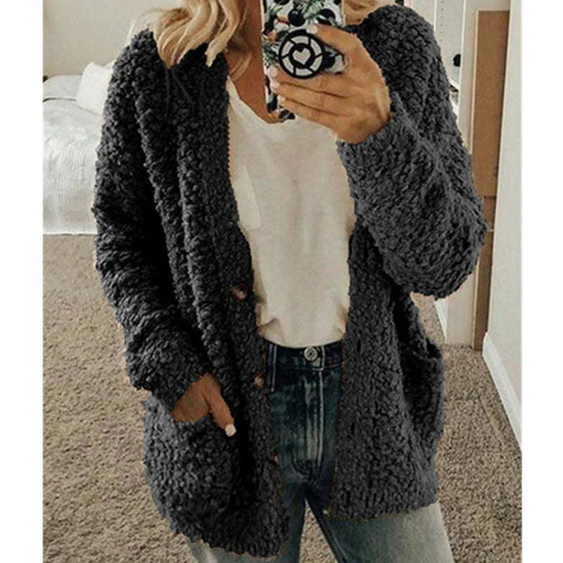 Femme portant un cardigan en tricot gris, t-shirt blanc et jean, tenant un smartphone. Mode automne-hiver, tenue décontractée et confortable.