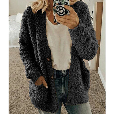 Femme portant un cardigan en tricot gris, t-shirt blanc et jean, tenant un smartphone. Mode automne-hiver, tenue décontractée et confortable.