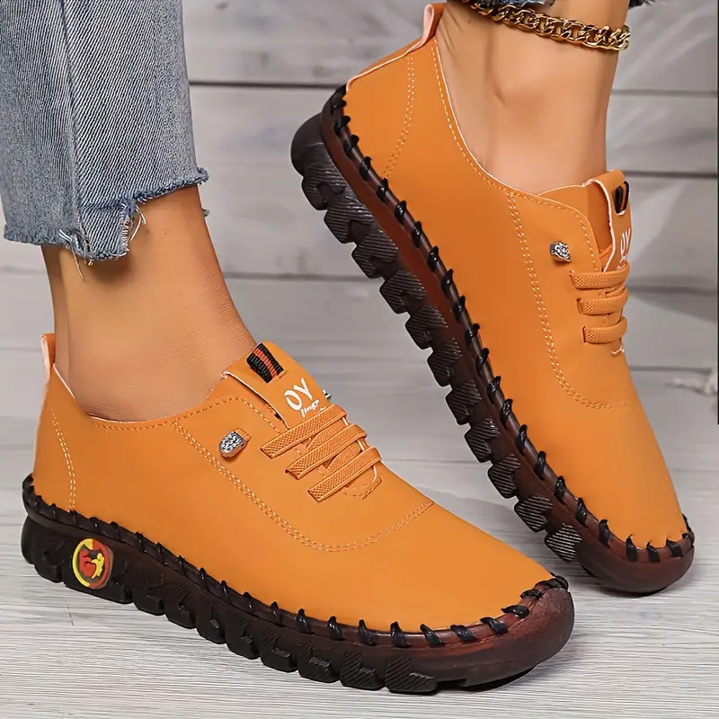 Chaussures de sport orange pour femme avec semelle épaisse noire, lacets assortis, portées avec un jean. Style décontracté et moderne.