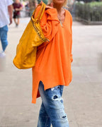 Femme en pull orange vif, jeans déchirés, portant un grand sac jaune. Mode décontractée, style urbain, tendance automne.