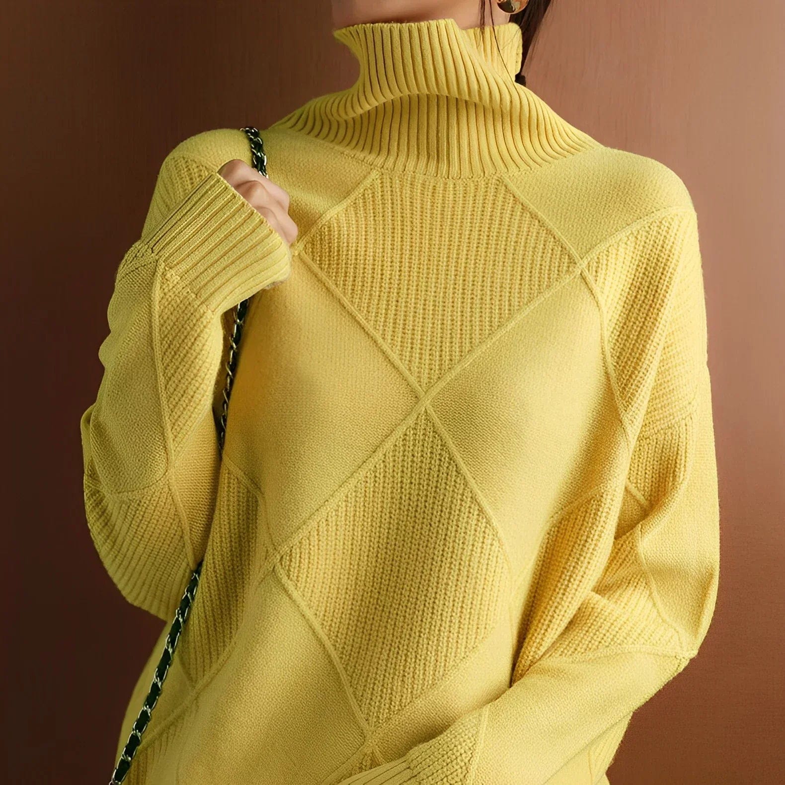 Femme portant un pull jaune à col roulé en maille texturée, motif losanges, manches longues, fond marron. Mode automne-hiver, style élégant.