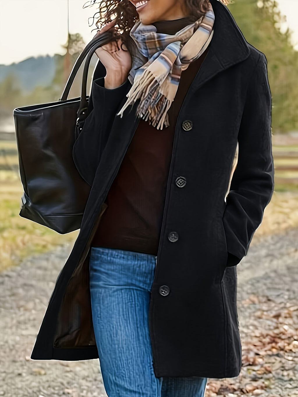 Femme portant un manteau noir élégant, écharpe à carreaux, sac à main en cuir noir, marchant en extérieur automnal. Mode hiver, style chic.