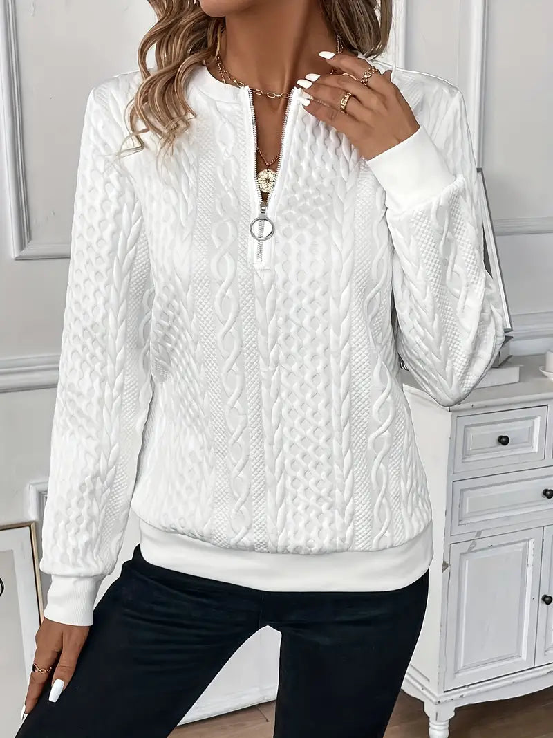 Femme portant un pull blanc à col zippé, motif torsadé, manches longues, devant un mur blanc. Mode automne-hiver, style élégant et décontracté.