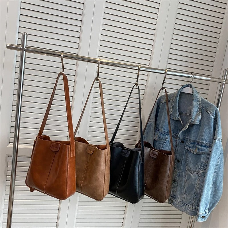 Quatre sacs à main en cuir marron et noir suspendus à une tringle à côté d'une veste en jean. Mode, accessoires, rangement.
