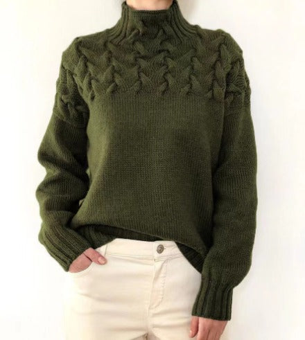 Pull vert en laine torsadée, col montant, manches longues, porté avec un pantalon beige. Mode automne-hiver, style décontracté et élégant.