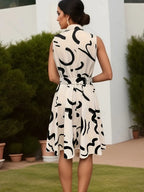 Robe d'été sans manches blanche à motifs noirs abstraits, femme de dos, jardin avec plantes en pot, style chic et moderne.