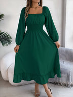 Robe longue verte à manches longues, col carré, portée par une femme. Style élégant et moderne, idéal pour occasions spéciales.