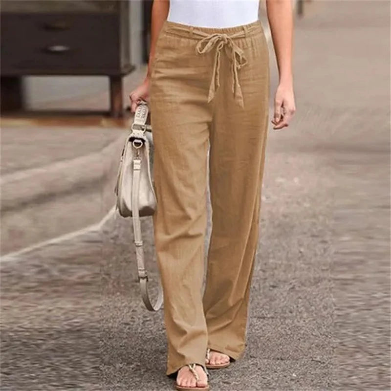 Pantalon large beige en lin pour femme, avec ceinture à nouer, porté avec un haut blanc. Mode décontractée, tendance estivale, confort élégant.