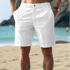 Short blanc en lin pour homme sur plage, style estival décontracté, idéal pour vacances, confort et élégance, fond mer et rochers.