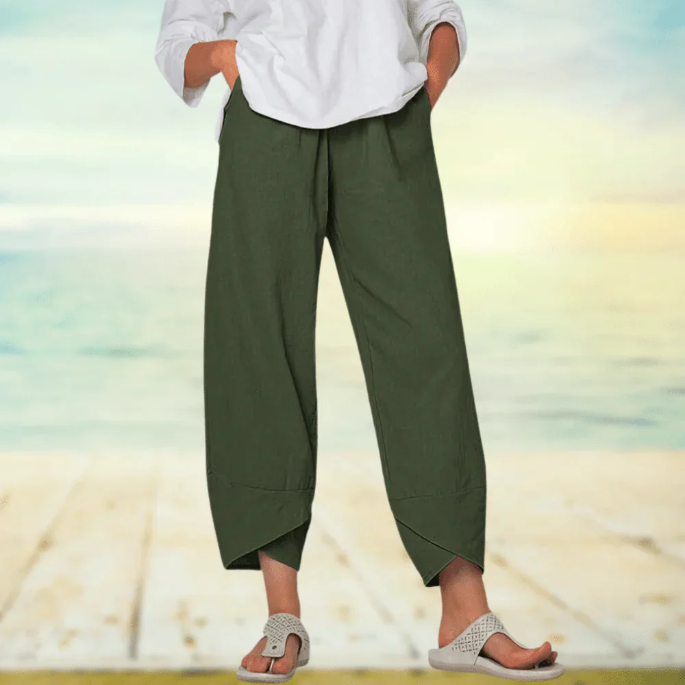 Pantalon large vert kaki en lin pour femme, style décontracté, porté avec un haut blanc et des sandales, sur fond de plage ensoleillée.