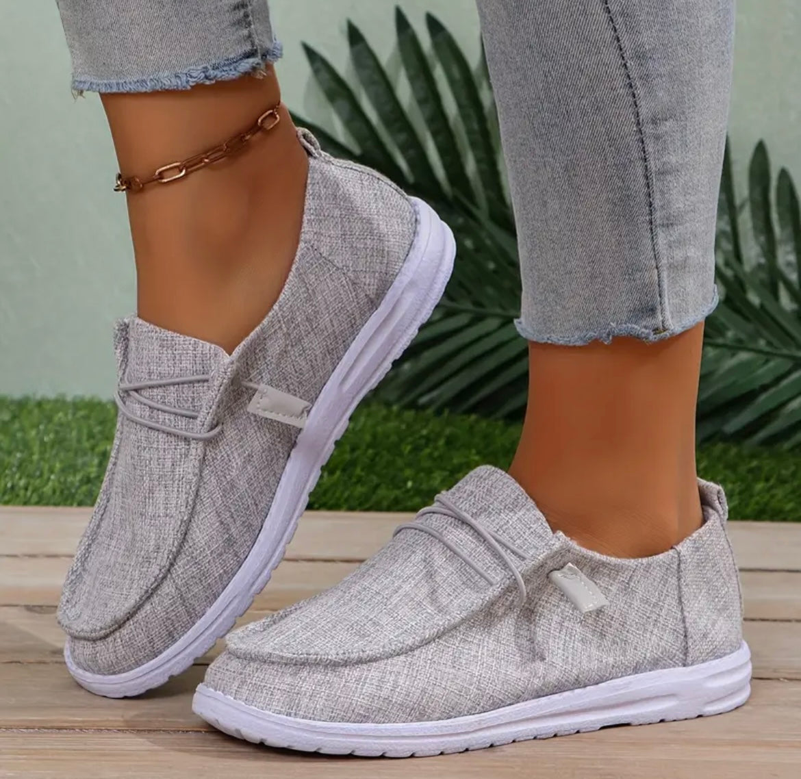 Chaussures décontractées en toile grise pour femme, portées avec un jean ajusté. Style moderne, semelle blanche, confort et élégance.