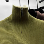 Pull en laine vert olive à col zippé, suspendu sur un cintre noir. Mode automne-hiver, vêtement chaud et élégant pour homme ou femme.