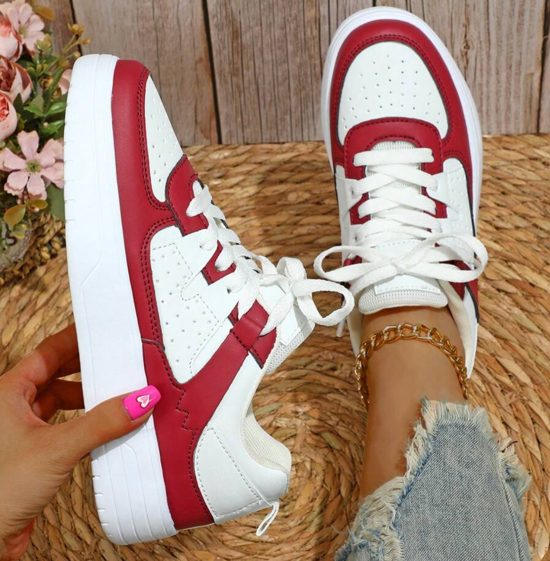 Chaussures de sport blanches et rouges sur fond de bois, portées avec un jean déchiré. Sneakers tendance, mode féminine, style décontracté.